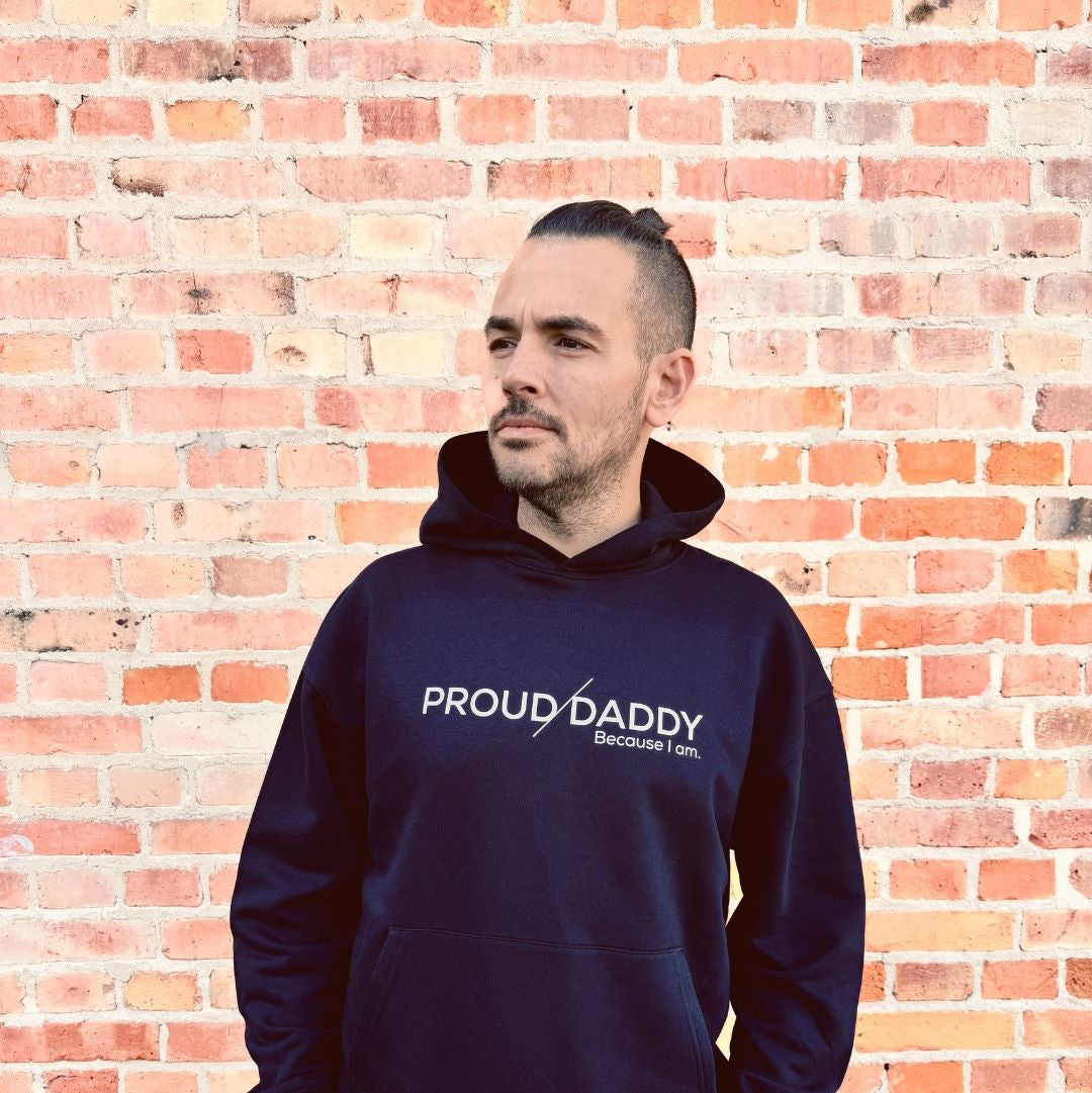 Mann vor Backsteinwand in schwarzem Hoodie mit Proud Daddy Audruck.